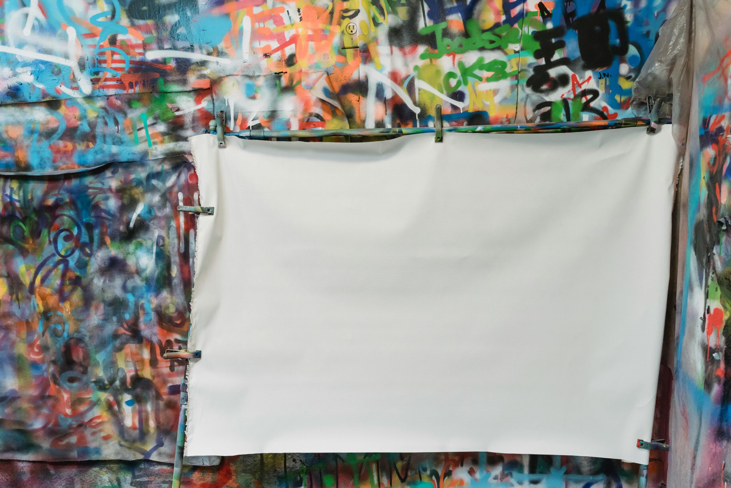 A vibrant graffiti wall with a blank white canvas in front for creative projects.